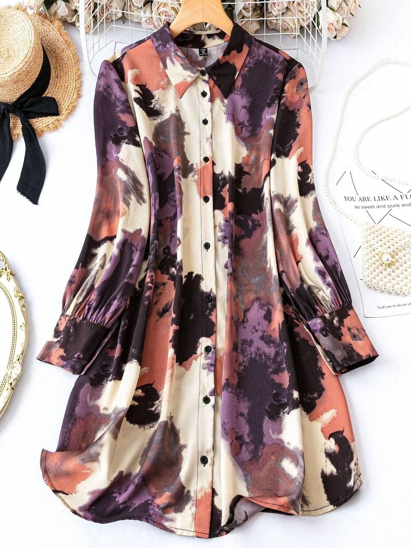 Burning Bones Geo Printed Tank Midi Dress displayed on wooden hanger against white backdrop with abstract watercolor-style pattern in purple, coral, and cream. Button-front dress features long sleeves with gathered cuffs and casual A-line silhouette in rayon fabric.