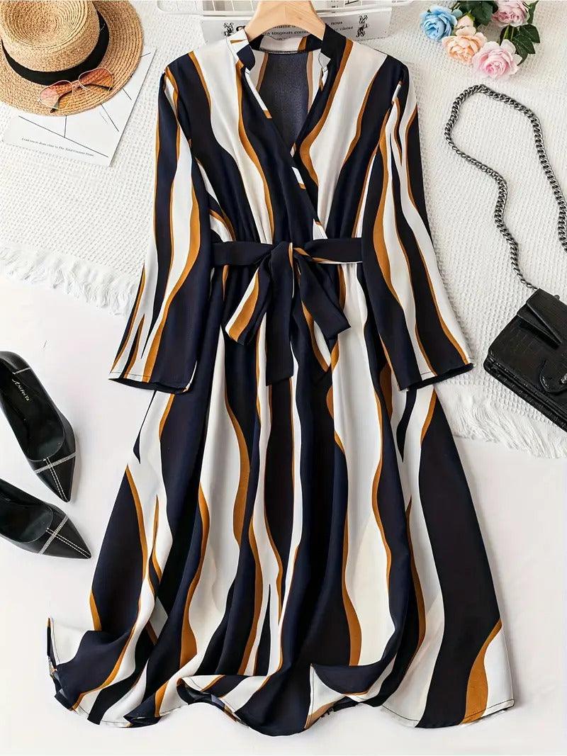 Burning Bones Abstract Print Surplice Neck Belted Dress styled in flatlay with navy, white, and caramel vertical stripes. Long-sleeve midi dress with wrap neckline and waist belt, shown alongside black pointed flats, straw hat, and decorative accessories on white background.